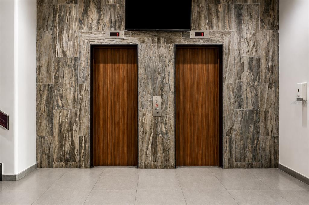 Two wood-paneled elevator doors are set into a wall covered in textured, gray stone tiles — 864 ASHFORD AVE. UNIT 712, SAN JUAN, PR