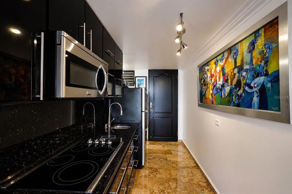 A galley kitchen features black cabinets, a stainless steel microwave, and tan stone flooring — 864 ASHFORD AVE. UNIT 712, SAN JUAN, PR