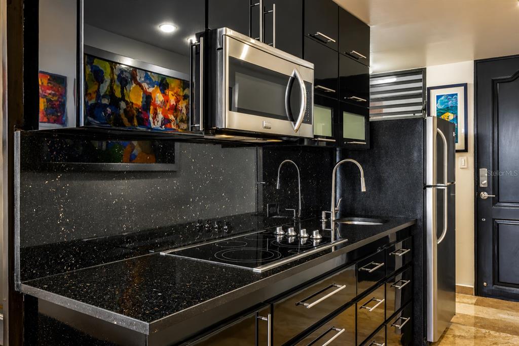 A modern kitchen features black glossy cabinets, a speckled countertop, and stainless steel appliances — 864 ASHFORD AVE. UNIT 712, SAN JUAN, PR