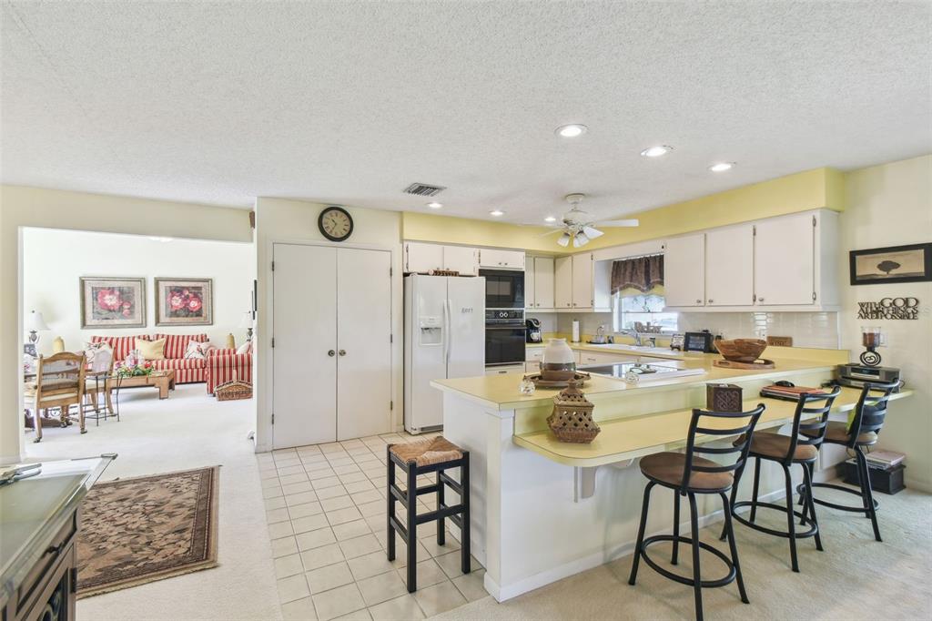 A kitchen with white cabinets, yellow countertops, and a breakfast bar overlooks a living area — 441 SAN JOSE DRIVE, WINTER HAVEN, FL