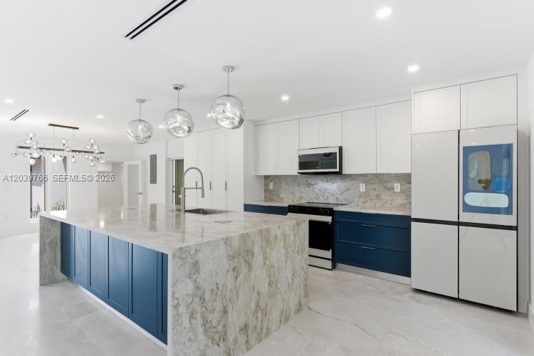 A modern kitchen features a large marble island, blue cabinetry, and stainless steel appliances — 291 E Shore Dr E, Miami FL 33133, MIAMI, FL