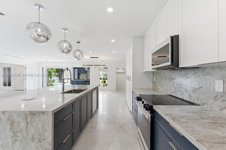 A modern kitchen features dark blue cabinetry, white marble countertops, and three glass pendant lights — 291 E Shore Dr E, Miami FL 33133, MIAMI, FL