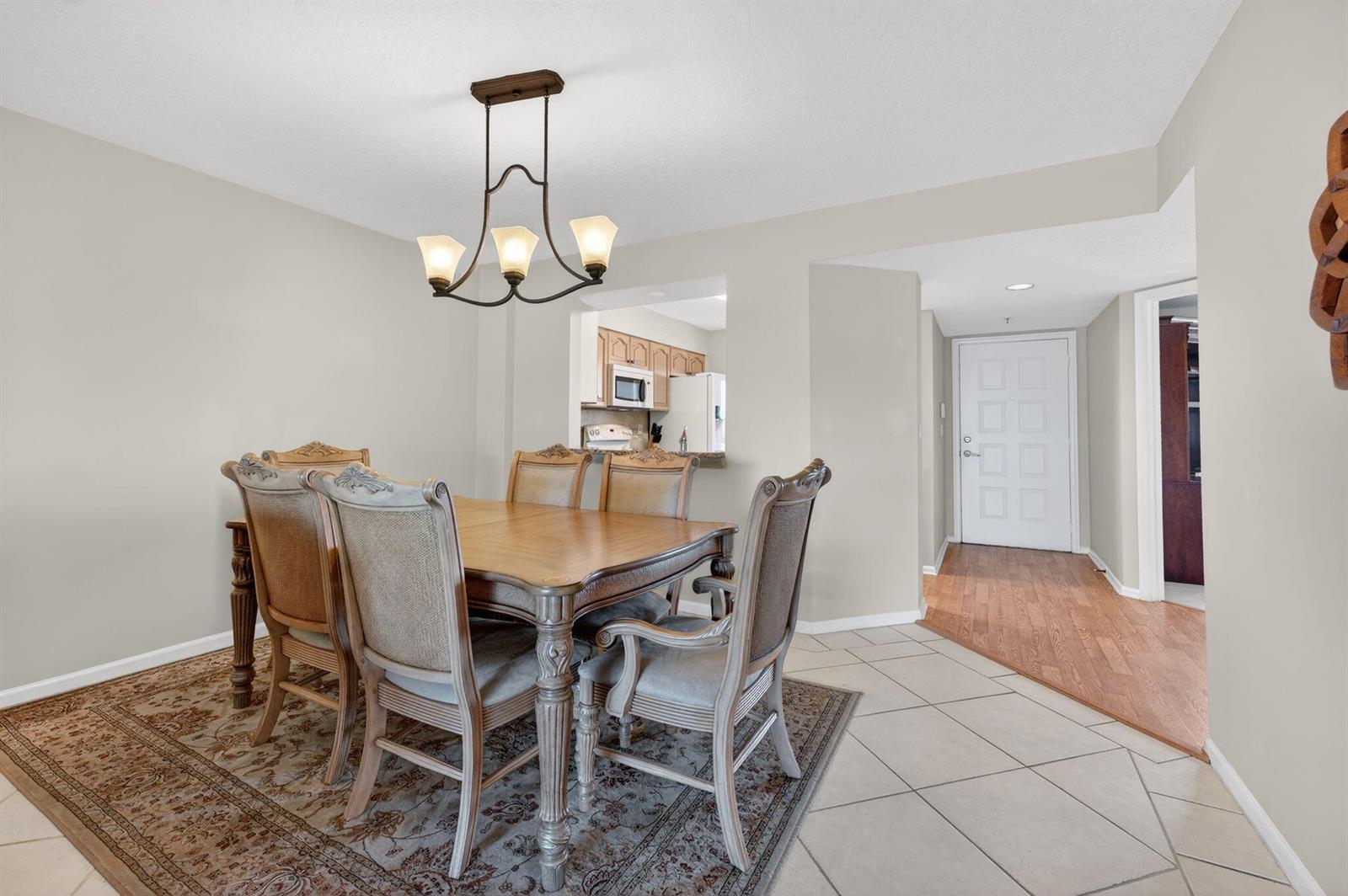 A dining area with a wooden table and chairs sits adjacent to a living room — 5906 Crystal Shores Drive # 404, Boynton Beach FL 33437, BOYNTON BEACH, FL