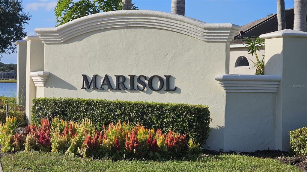 A beige stucco entrance sign for Marisol sits behind a bed of colorful flowers — 552 CARO COURT, NEW SMYRNA BEACH, FL