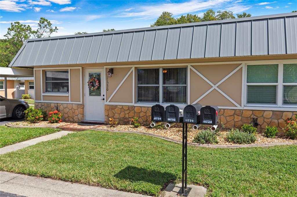 A single-story building exterior features a metal roof, stone base, and a row of mailboxes — 11730 CARISSA LANE UNIT 0, NEW PORT RICHEY, FL