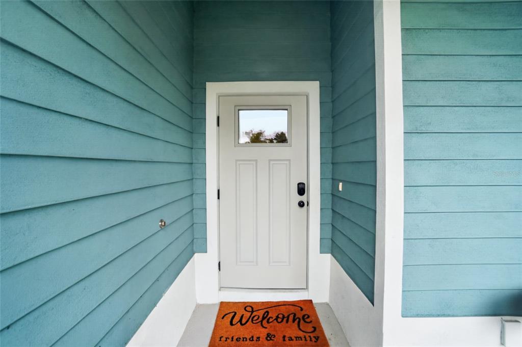 A white front door with a small window is set between blue horizontal siding walls — 21434 DEKALS AVENUE, PORT CHARLOTTE, FL