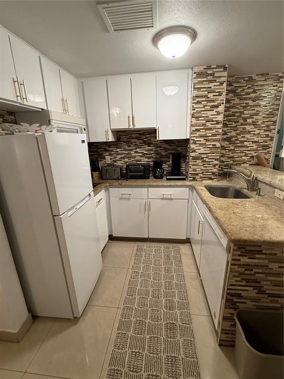 A kitchen features white cabinets, granite countertops, a tiled backsplash, and stainless steel appliances — 6165 CARRIER DRIVE UNIT 2404, ORLANDO, FL