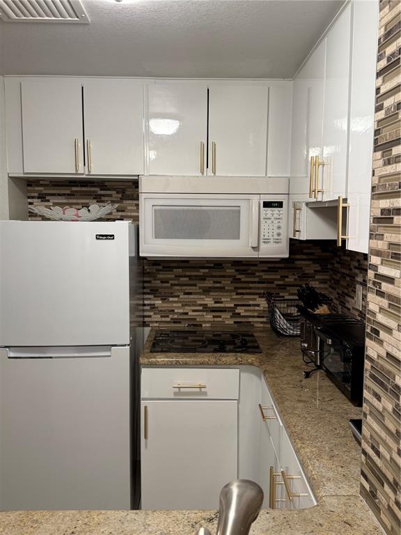 A kitchen features white cabinets, gold hardware, a granite countertop, and a tiled backsplash — 6165 CARRIER DRIVE UNIT 2404, ORLANDO, FL