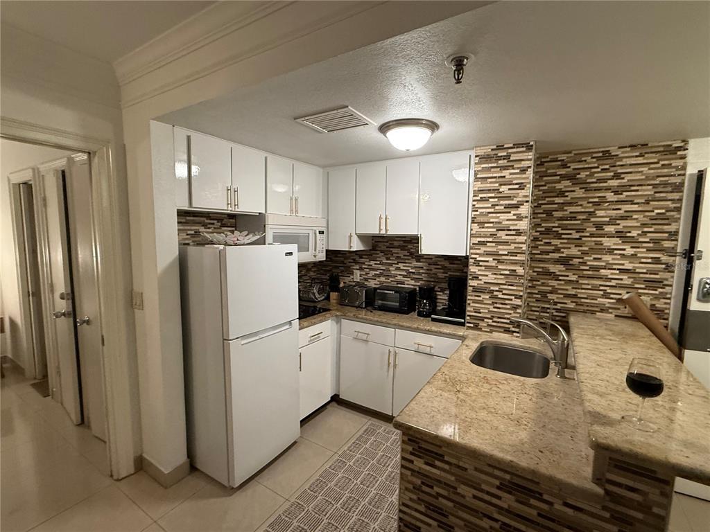 A kitchen features white cabinets, a white refrigerator, granite countertops, and a tiled backsplash — 6165 CARRIER DRIVE UNIT 2404, ORLANDO, FL