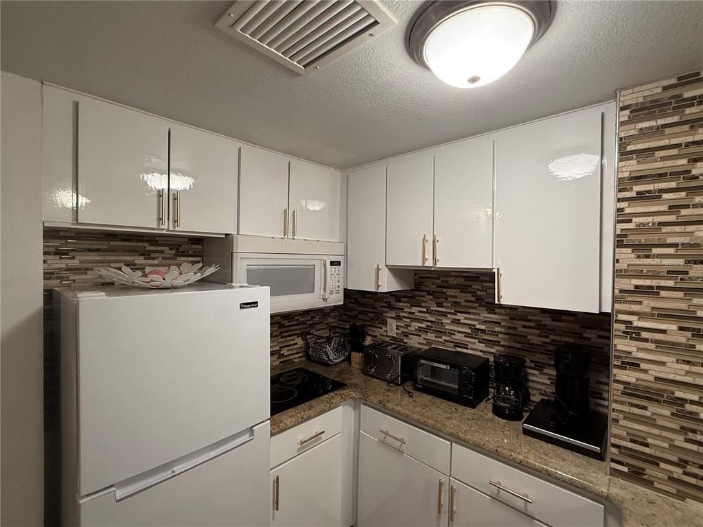 A kitchen features white cabinets, a granite countertop, a tiled backsplash, and white appliances — 6165 CARRIER DRIVE UNIT 2404, ORLANDO, FL