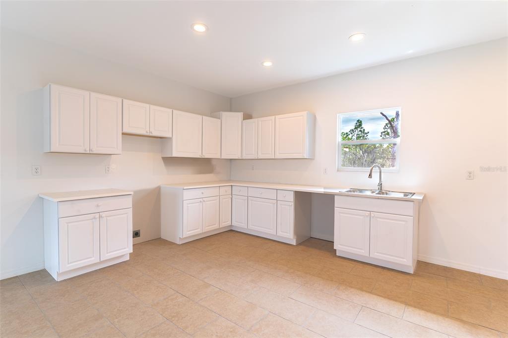 A kitchen features white cabinets, light-colored countertops, a sink, and beige tile flooring — 1417 BITTERSWEET STREET, LAKE PLACID, FL