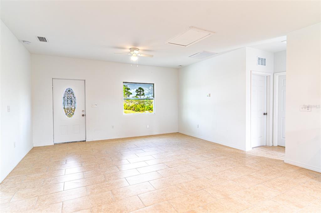 A bright, empty room features white walls, tan tile flooring, a ceiling fan, and a door — 1417 BITTERSWEET STREET, LAKE PLACID, FL