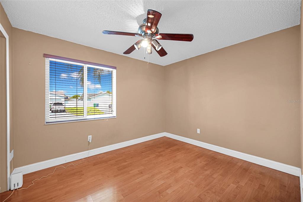 An empty bedroom with tan walls, wood-look flooring, a ceiling fan, and a window — 26543 SW 122ND PLACE, HOMESTEAD, FL