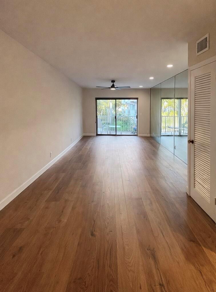 An empty living room features wood-look flooring, a ceiling fan, and a mirrored accent wall — 311 E Ocean Avenue # 205, Lantana FL 33462, LANTANA, FL