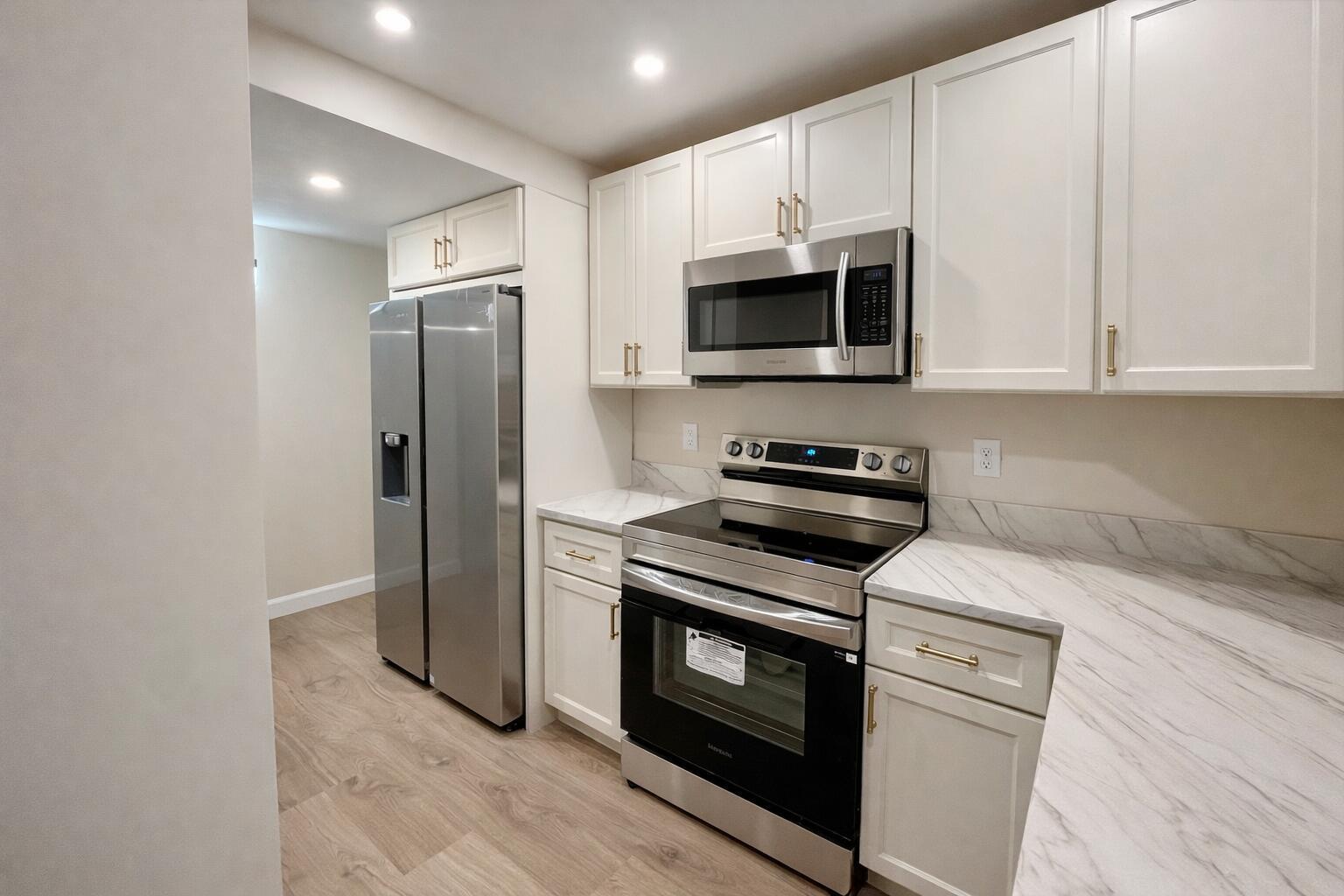 A kitchen features white cabinets, stainless steel appliances, and marble-patterned countertops — 311 E Ocean Avenue # 205, Lantana FL 33462, LANTANA, FL