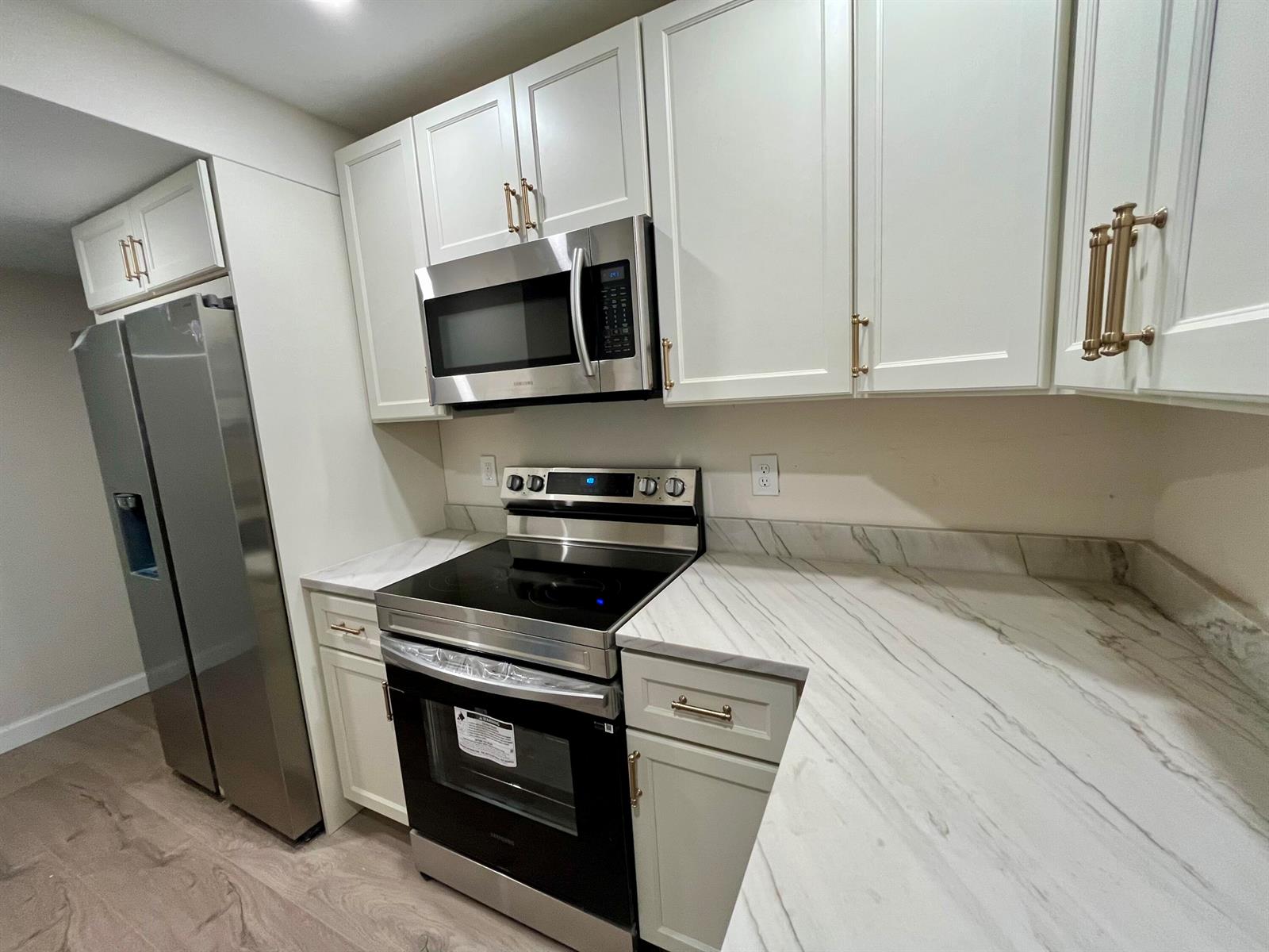 A kitchen features white cabinets, stainless steel appliances, and marble-patterned countertops — 311 E Ocean Avenue # 205, Lantana FL 33462, LANTANA, FL