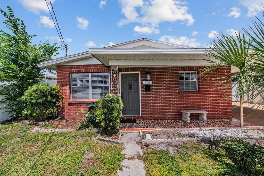 A single-story brick house features a covered front porch, a gray door, and landscaping — 2709 W ABDELLA STREET, TAMPA, FL