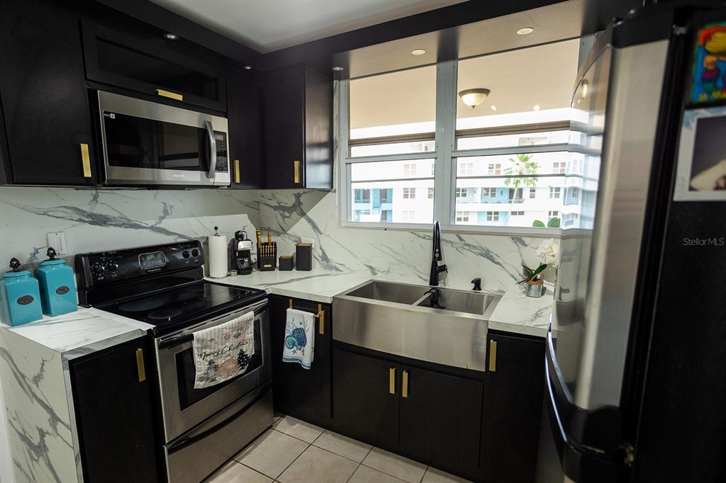 A kitchen features dark cabinets, stainless steel appliances, a farmhouse sink, and marble-patterned countertops — 686 PUERTO NUEVO UNIT 364, VEGA BAJA, PR