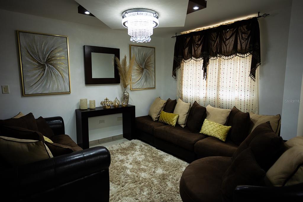 A living room features brown sofas, a shaggy rug, a crystal chandelier, and wall art — 686 PUERTO NUEVO UNIT 364, VEGA BAJA, PR