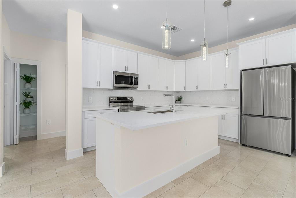 A modern kitchen features white cabinets, stainless steel appliances, a center island, and tile flooring — 162 APOLLO DRIVE, ROTONDA WEST, FL