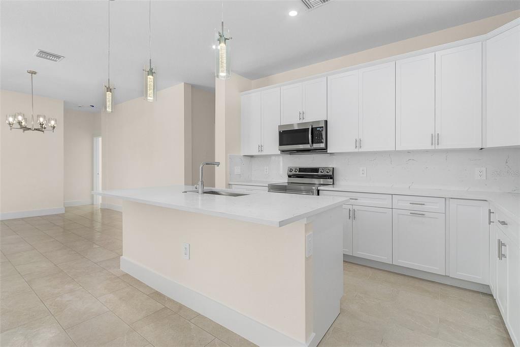 A modern kitchen features white cabinets, a central island with a sink, and stainless appliances — 162 APOLLO DRIVE, ROTONDA WEST, FL