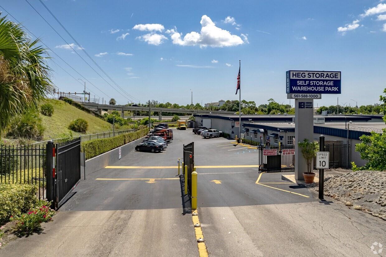 An asphalt driveway leads through an open gate into a self-storage facility parking lot — 1800 Hypoluxo Road, Lake Worth FL 33462, LAKE WORTH, FL