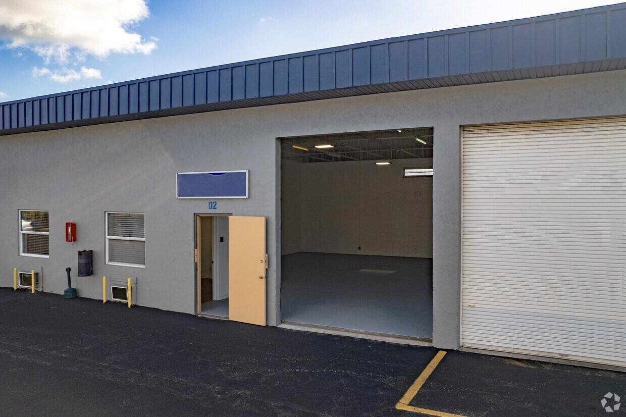 An exterior view of a commercial warehouse unit with a roll-up door and entrance — 1800 Hypoluxo Road, Lake Worth FL 33462, LAKE WORTH, FL