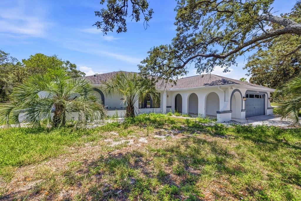 A single-story house with a white exterior, arched entryways, and a garage under large trees — 10186 SLEEPY WILLOW COURT, SPRING HILL, FL