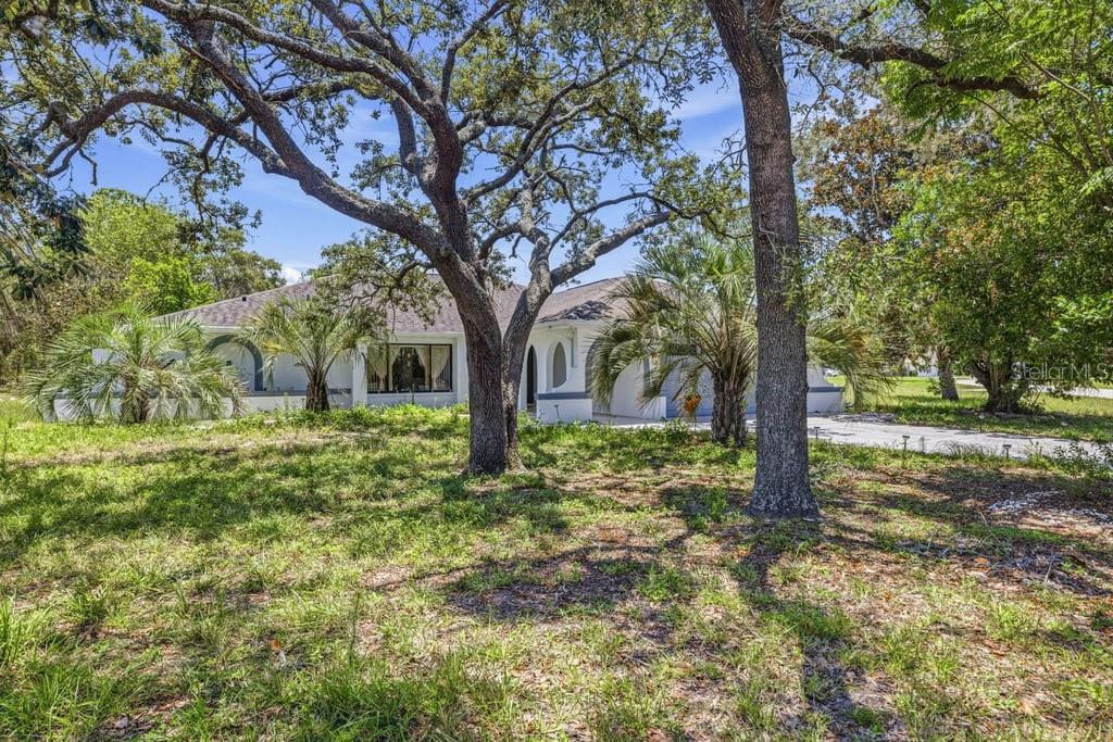 A single-story white house with arched windows is surrounded by large trees and landscaping — 10186 SLEEPY WILLOW COURT, SPRING HILL, FL