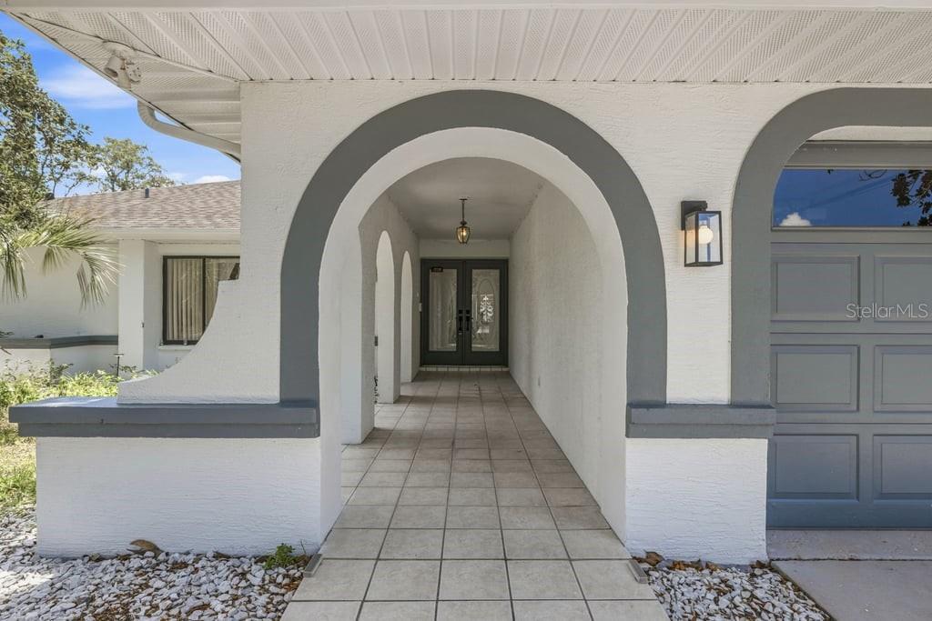 A covered entryway features a tiled walkway leading to double front doors under arched openings — 10186 SLEEPY WILLOW COURT, SPRING HILL, FL