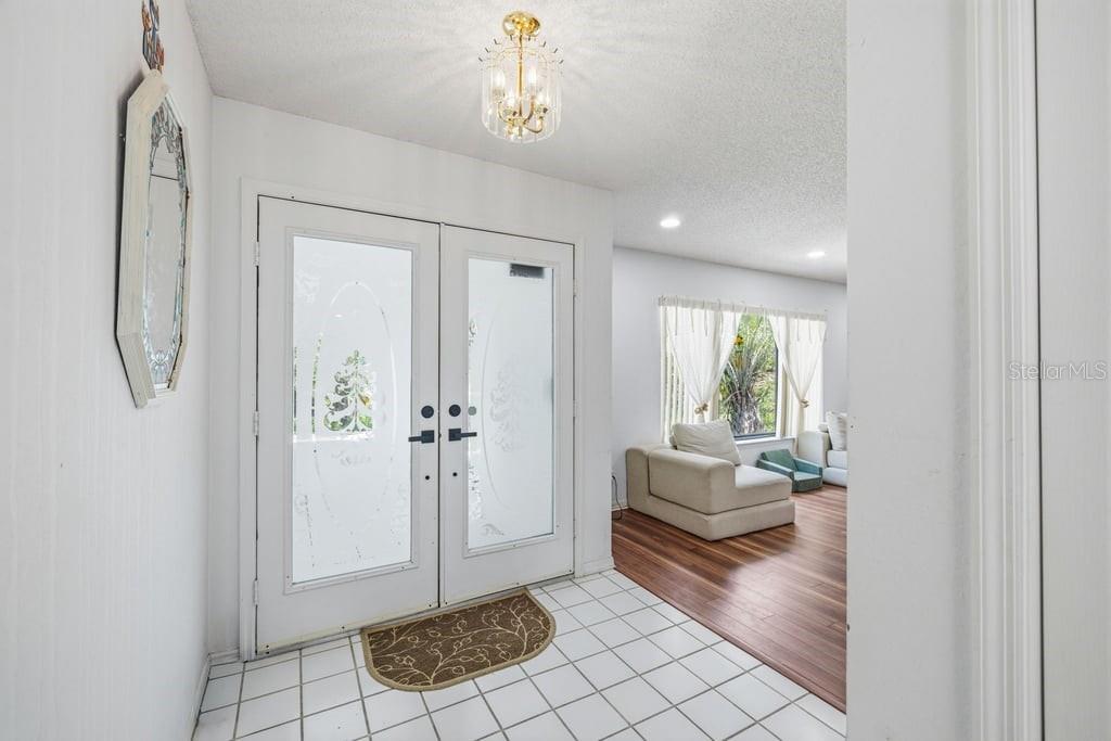 An entryway features white tile flooring, double glass-paneled doors, and a crystal chandelier — 10186 SLEEPY WILLOW COURT, SPRING HILL, FL