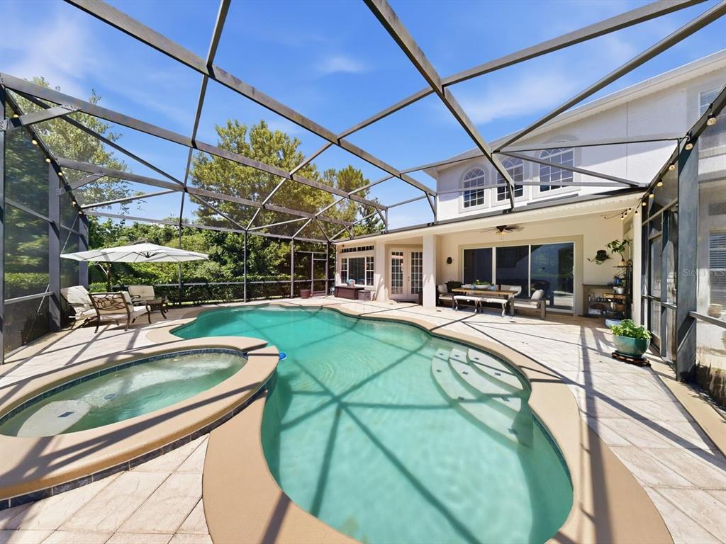 A screened-in pool and spa area with a patio and house exterior in the background — 561 HARRISWOOD COURT, DAVENPORT, FL