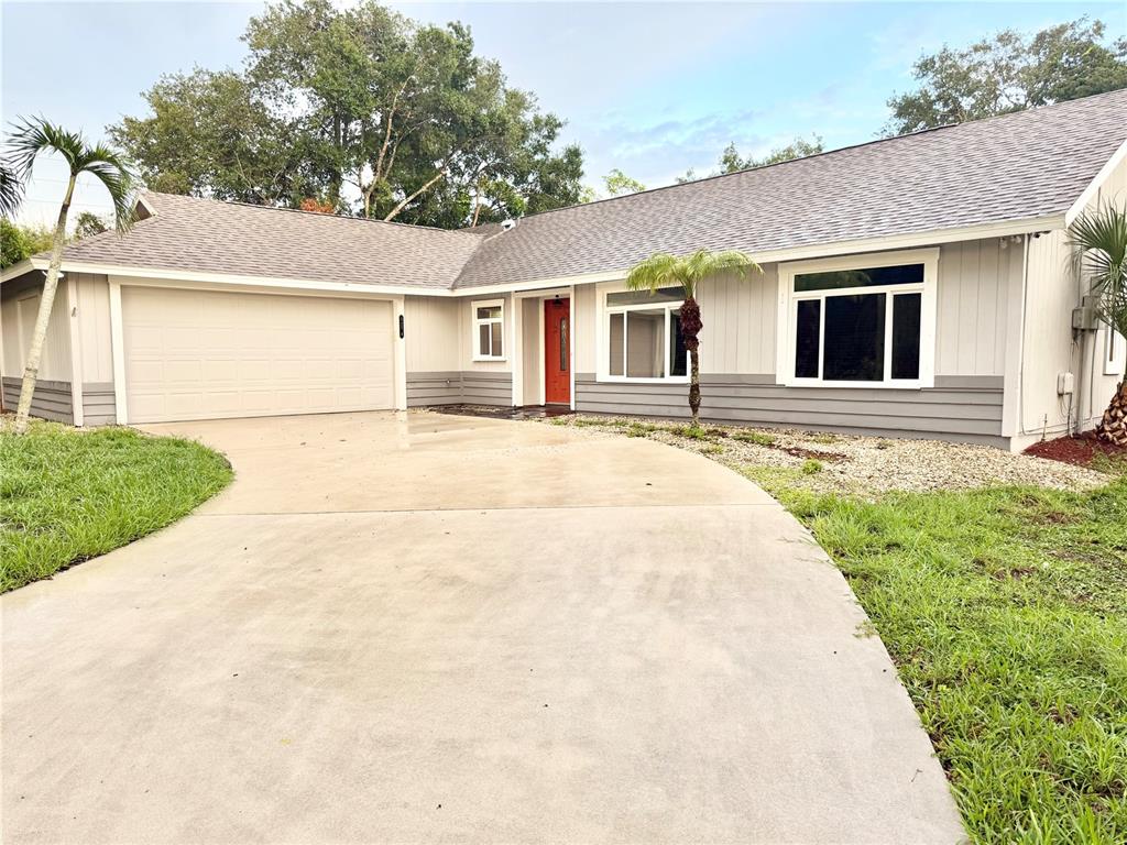 A single-story house with a two-car garage, gray siding, and a bright red front door — 5274 CEDAR HAMMOCK COURT, SARASOTA, FL