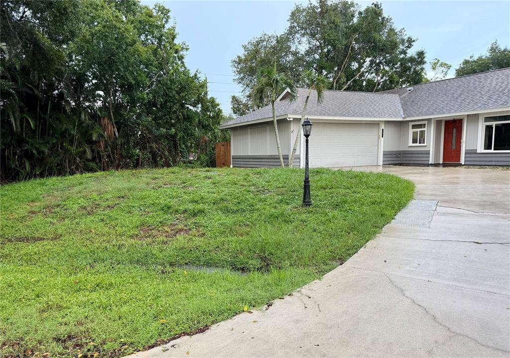 A grassy front yard leads to a single-story house with a garage and red door — 5274 CEDAR HAMMOCK COURT, SARASOTA, FL