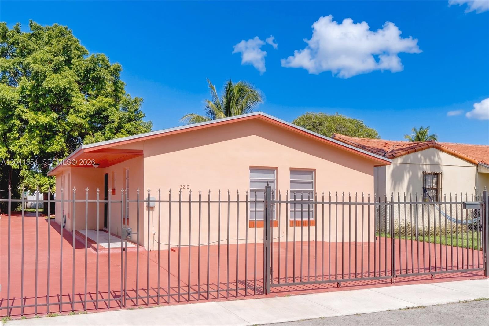 A peach-colored single-story house features a metal fence and a red paved front yard — 3210 NW 19th St, Miami FL 33125, MIAMI, FL