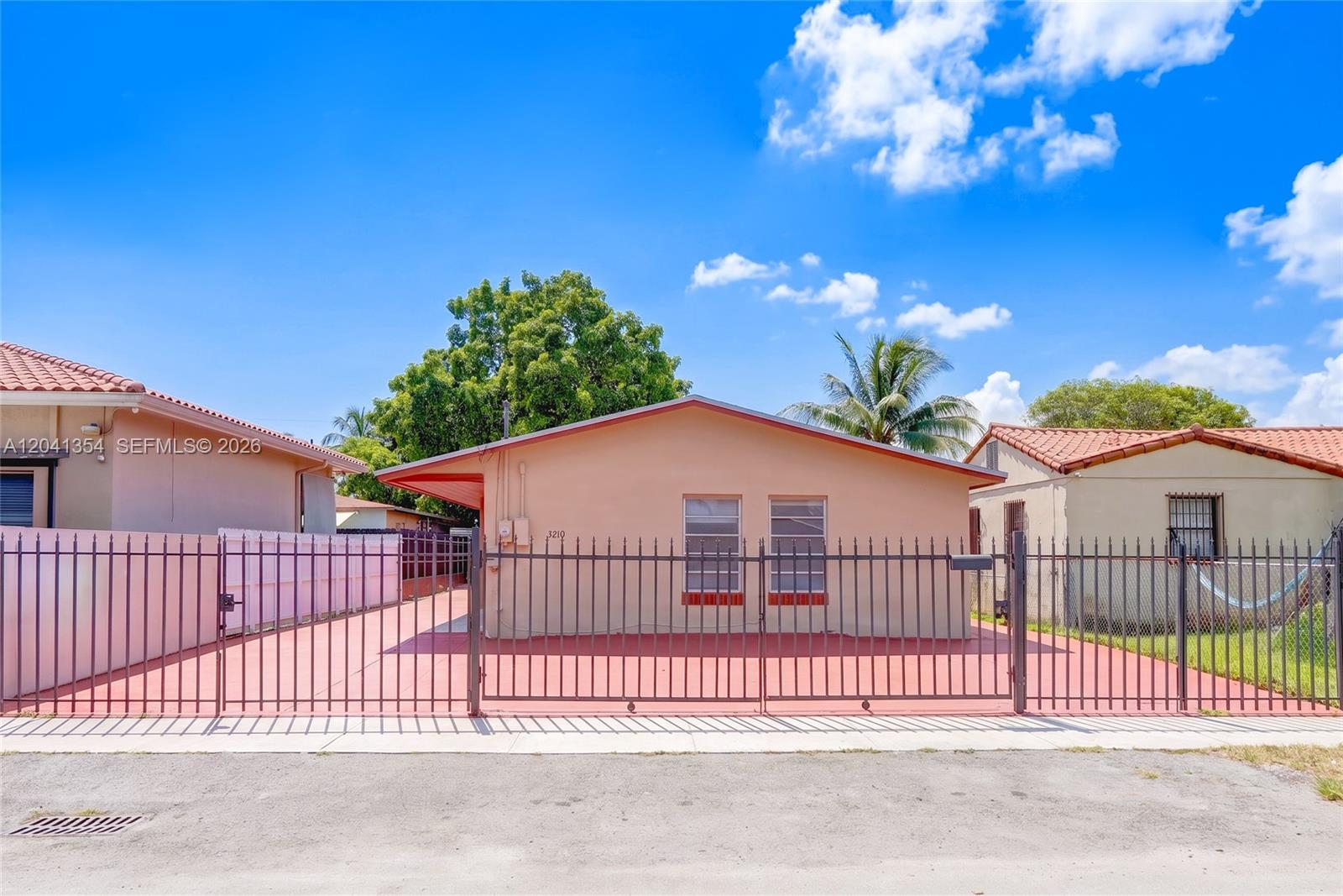 A single-story peach-colored house features a metal fence enclosing a paved front yard — 3210 NW 19th St, Miami FL 33125, MIAMI, FL