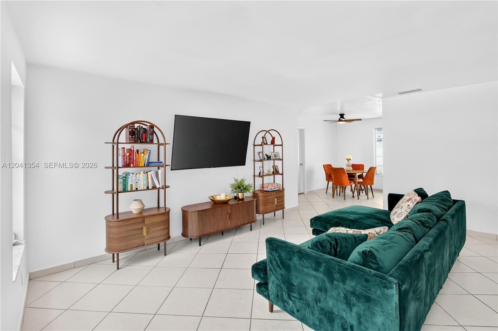 A living room features a green velvet sofa, a television, and wooden shelving units — 3210 NW 19th St, Miami FL 33125, MIAMI, FL