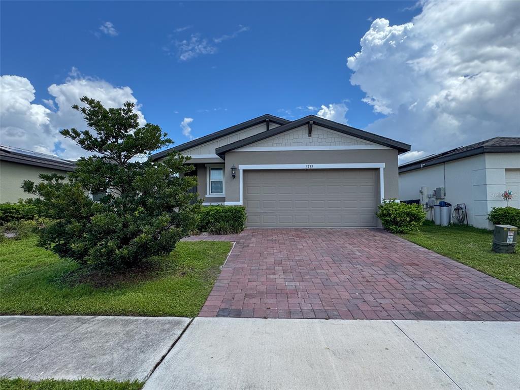 A single-story house with a beige exterior, a two-car garage, and a brick paver driveway — 3533 BROADWING BOULEVARD, POINCIANA, FL
