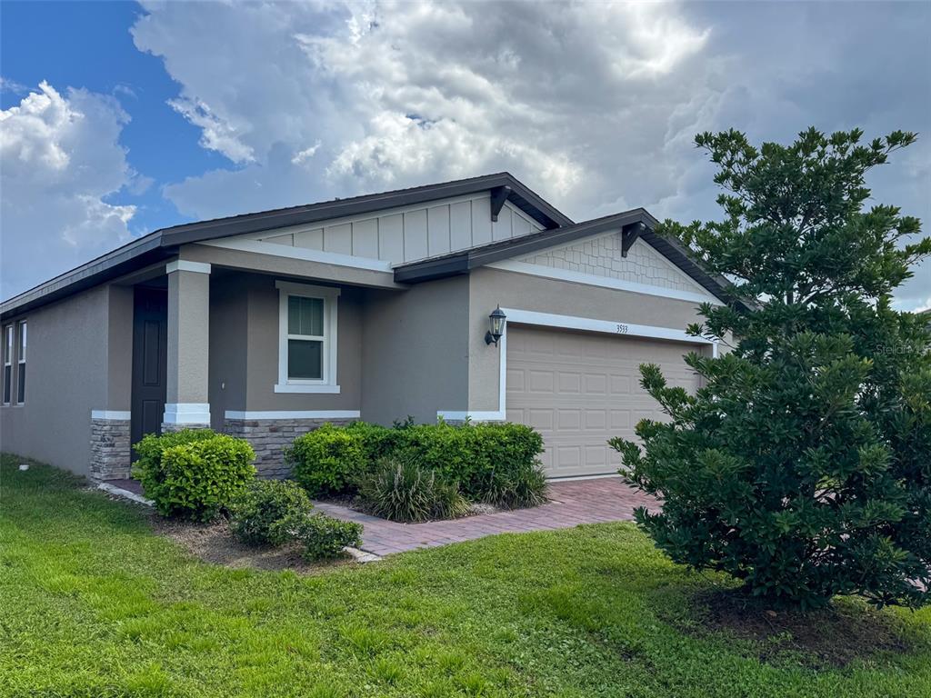A single-story house with a beige stucco exterior, stone accents, and a two-car garage — 3533 BROADWING BOULEVARD, POINCIANA, FL
