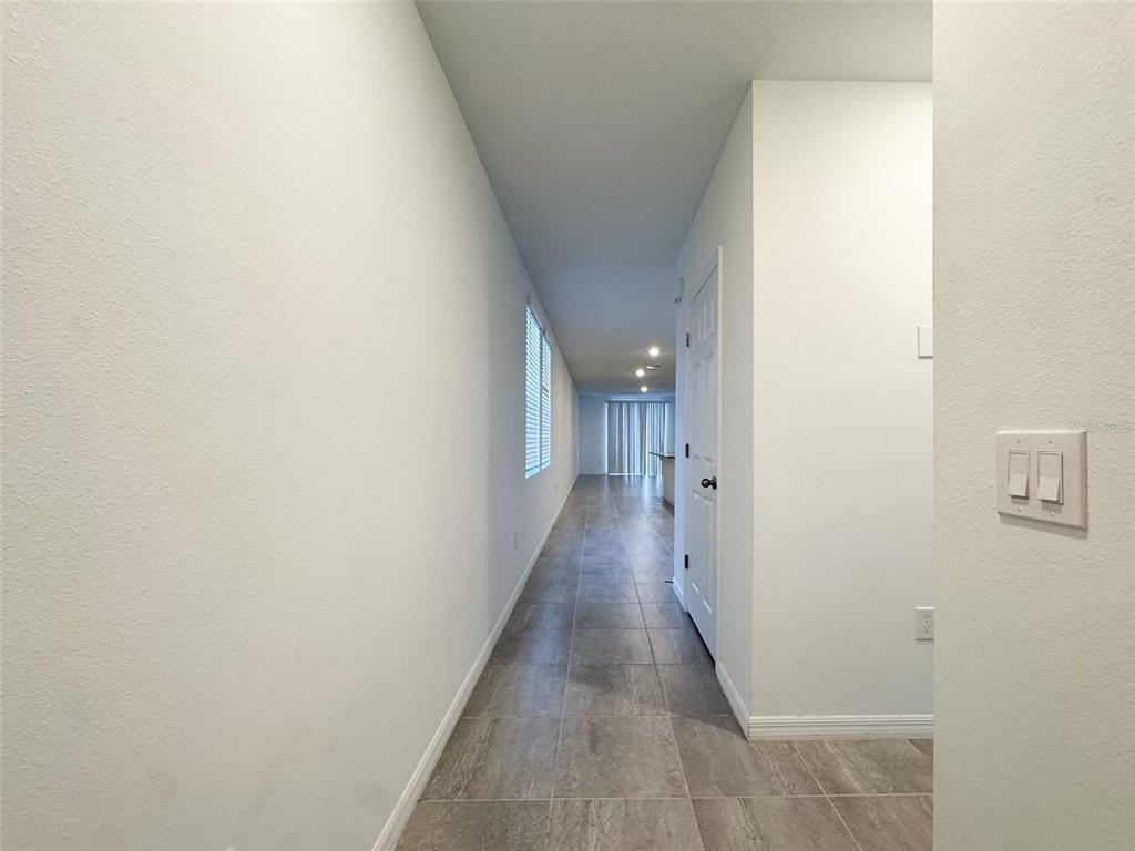 A long hallway with gray tile flooring leads toward a bright room with sliding doors — 3533 BROADWING BOULEVARD, POINCIANA, FL