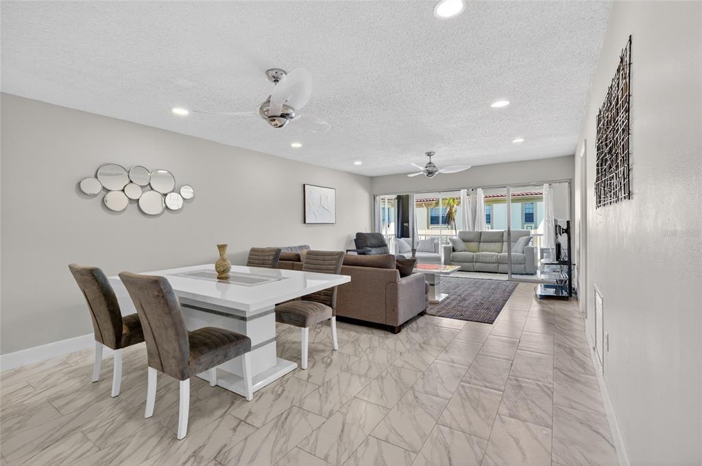 An open-concept living and dining area features tile flooring, a white table, and sliding doors — 19029 US HIGHWAY 19 N UNIT 6-16, CLEARWATER, FL