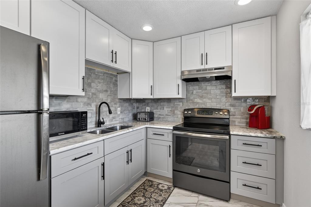 A kitchen with white cabinets, gray subway tile backsplash, stainless appliances, and marble-look countertops — 19029 US HIGHWAY 19 N UNIT 6-16, CLEARWATER, FL