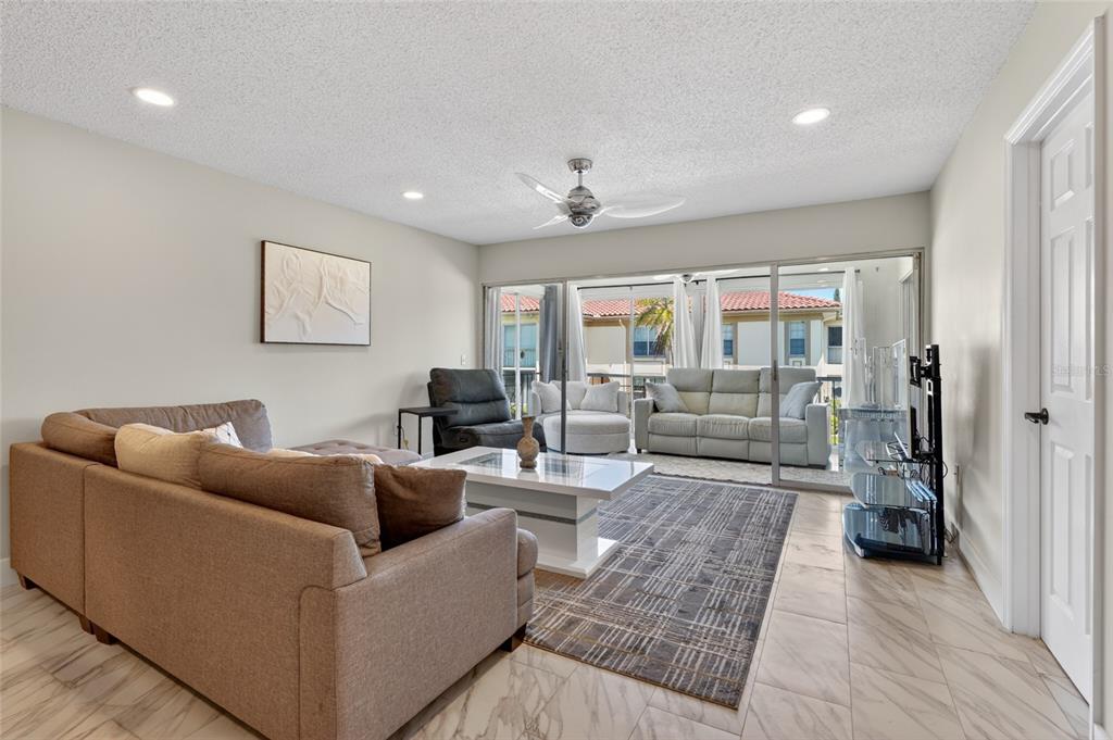 A living room features a sectional sofa, a coffee table, and sliding doors to a balcony — 19029 US HIGHWAY 19 N UNIT 6-16, CLEARWATER, FL