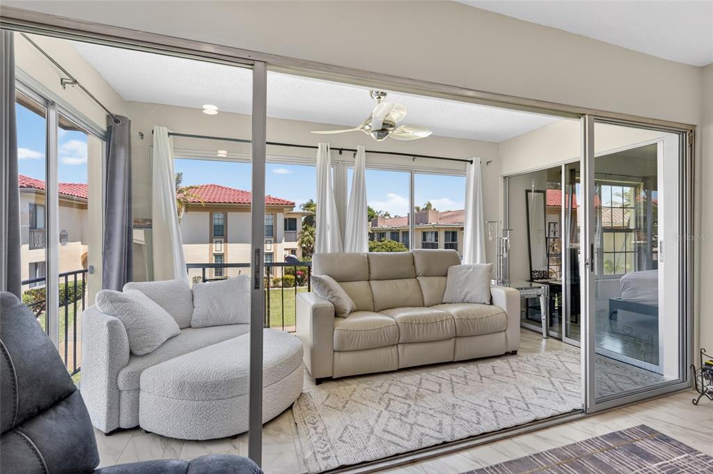 A sunroom with a white sofa, a round chair, and sliding glass doors overlooking apartments — 19029 US HIGHWAY 19 N UNIT 6-16, CLEARWATER, FL