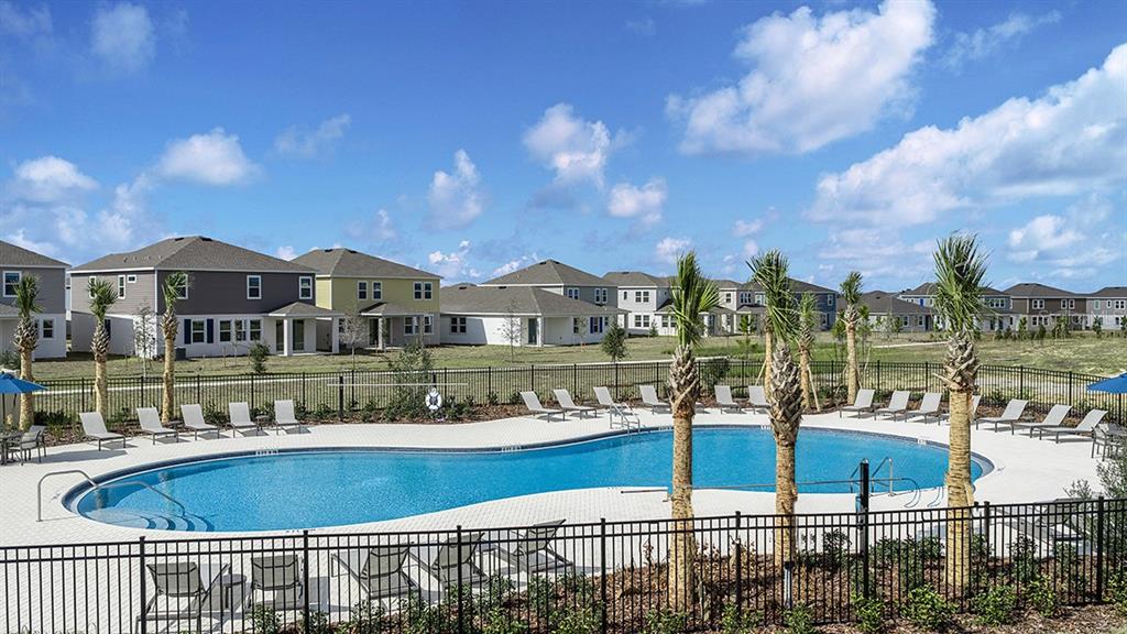 A swimming pool with lounge chairs is surrounded by a black fence and suburban houses — 233 STREAMWATER WAY, GROVELAND, FL