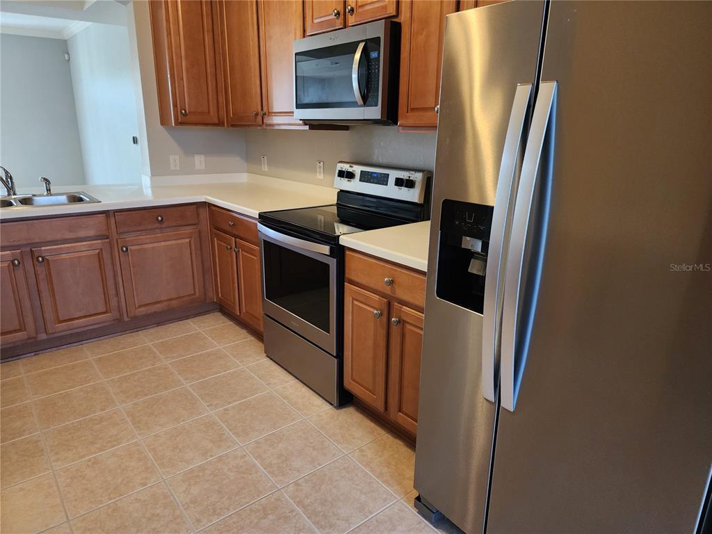 A kitchen features wood cabinets, stainless steel appliances, and light-colored countertops — 1211 STONECUTTER DRIVE UNIT 403, CELEBRATION, FL