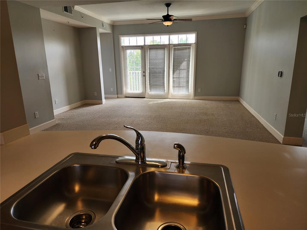 A stainless steel double kitchen sink overlooks a carpeted living area with glass patio doors — 1211 STONECUTTER DRIVE UNIT 403, CELEBRATION, FL