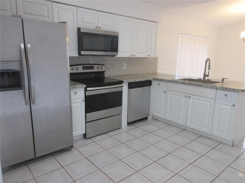 A kitchen features white cabinets, stainless steel appliances, granite countertops, and light-colored tile flooring — 14131 SW 30TH TERRACE ROAD, OCALA, FL