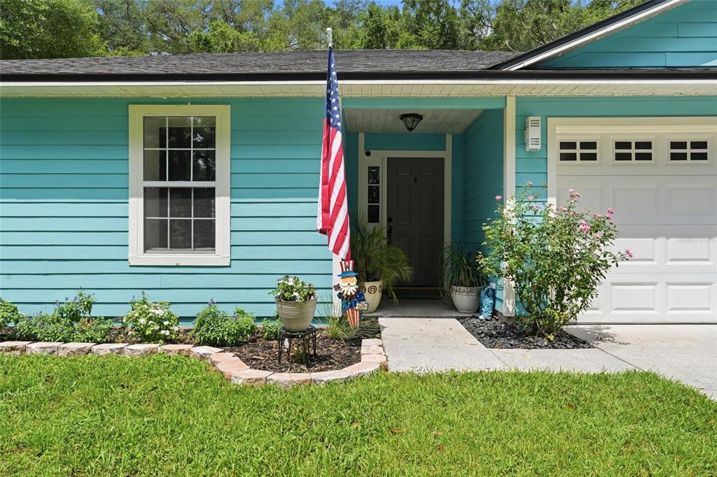 A teal house exterior features a front door, a garage, and a small garden bed — 17686 NW 239TH TERRACE, HIGH SPRINGS, FL