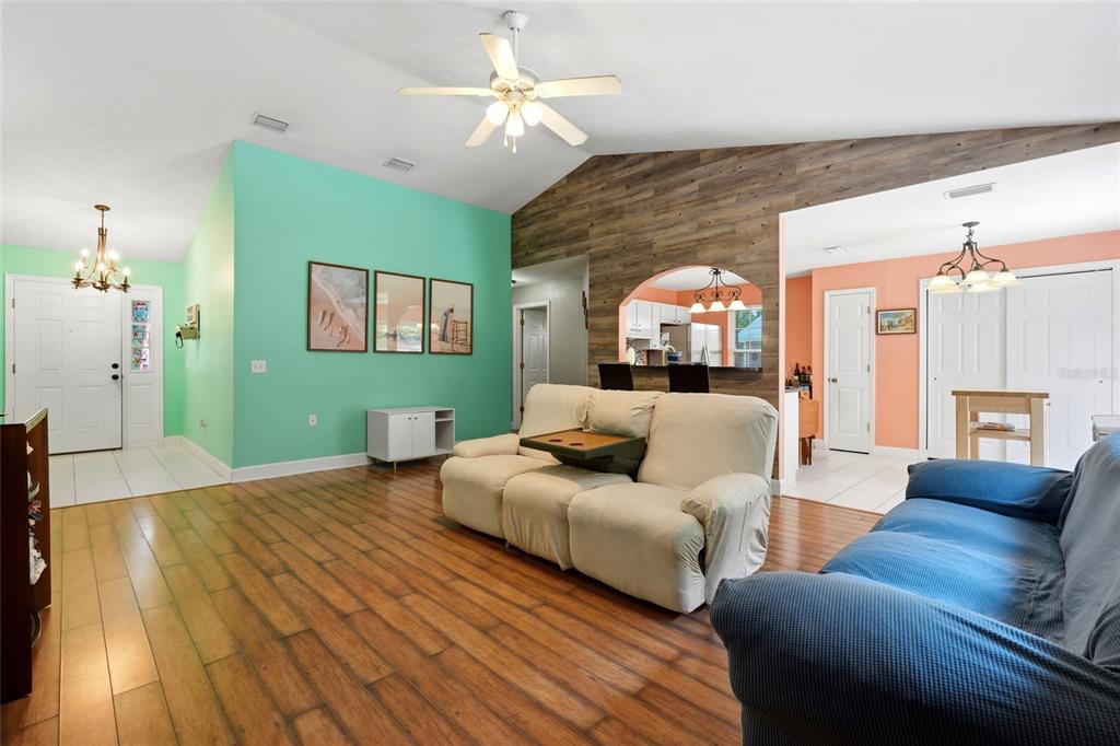 A living room features wood-look flooring, a vaulted ceiling, and a wood-paneled accent wall — 17686 NW 239TH TERRACE, HIGH SPRINGS, FL